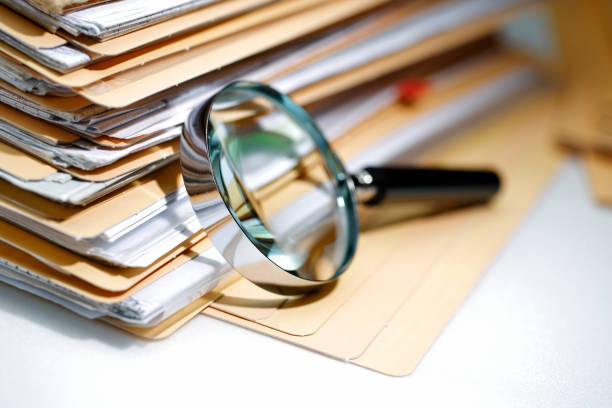 Stack of manila folders filled with papers and a magnifying glass resting against the edge of the stack