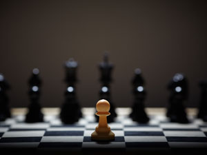 Chess board with single pawn in the foreground alone versus all the opponent's chess pieces in the background